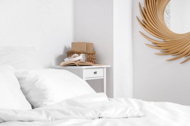 Rahat bir yatak, açık yatak odasında kitaplar ve kulaklıklar olan bir masa.