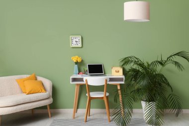 Yeşil duvarda işyeri, ev bitkisi, kanepe ve saati olan şık bir ofis.