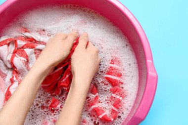 Elbiseleri mavi arka planda plastik leğende yıkayan kadın.