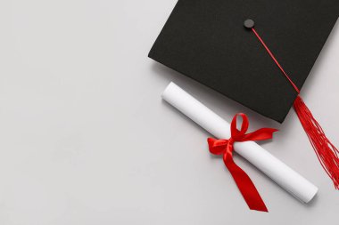 Kırmızı kurdeleli diploma ve beyaz arka planda mezuniyet şapkası.