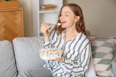 Evdeki kanepede dondurma yiyen genç bir kadın.