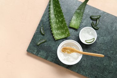 Bej arka planda yaprakları olan bir kase aloe vera jel ve pano.