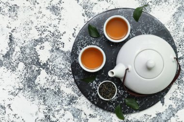 Arkaplanda kurumuş yapraklarla dolu sıcak çay kaseleri ve çaydanlık.