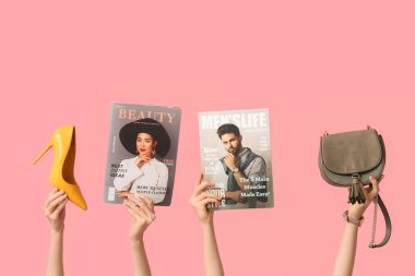 Farklı dergilere sahip kadın elleri, pembe arka planda yüksek topuklu ve şık bir çanta.