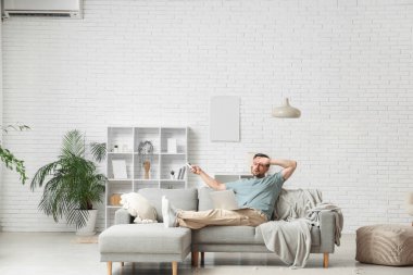 Evde dizüstü bilgisayar kullanırken klimayı açan yakışıklı genç adam.