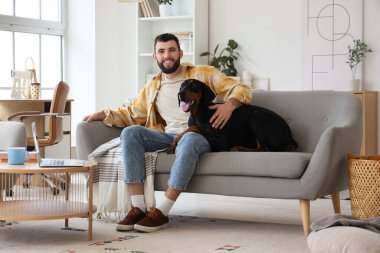 Dobermann 'ın köpeği evdeki kanepede oturan genç adam.