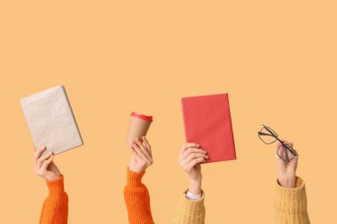 Kitapları, gözlükleri ve sarı arka planda bir fincan kahveyi olan kadın elleri.