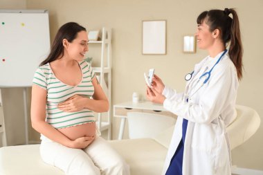 Kadın doktor klinikteki hamile kadına tükenmez kalemle glukometre veriyor.