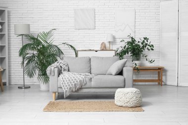 Beyaz tuğla duvarın yanında kanepesi ve çiçekleri olan aydınlık oturma odasının içinde.