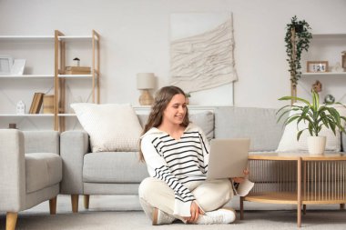 Oturma odasında dizüstü bilgisayar kullanan genç bir kadın.