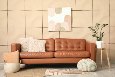 Pouf ve deri kahverengi kanepe oturma odasının iç tarafındaki bej fayans duvarının yanında.