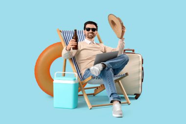 Mavi arka planda dizüstü bilgisayarı ve bira olan genç bir iş adamı. Yaz tatili kavramı