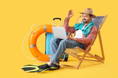 Dizüstü bilgisayarlı genç işadamı güverte sandalyesinde ve sarı arka planda plaj aksesuarlarında iyi görünüyor. Yaz tatili kavramı