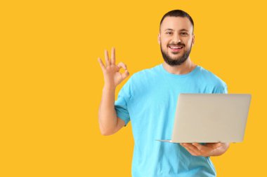 Laptoplu yakışıklı genç adam sarı arka planda iyi bir hareket gösteriyor.