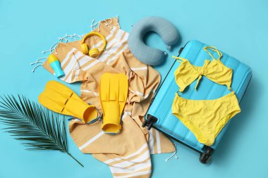 Mavi arka planda bavul, mayo, raket ve plaj aksesuarlarıyla kompozisyon