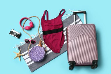 Mavi arka planda bavul, mayo, kulaklık ve plaj aksesuarlarıyla kompozisyon