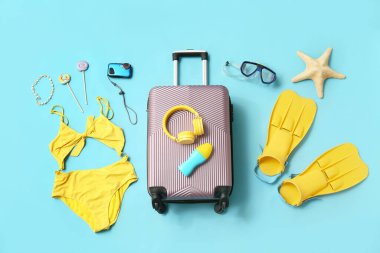 Bavul, mayo, kulaklık, fotoğraf makinesi ve mavi arka planda plaj aksesuarları.