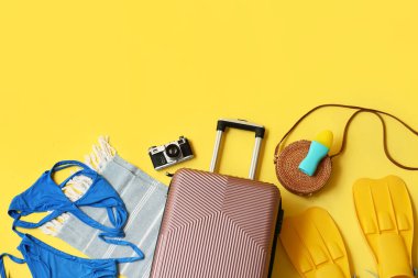 Çantalı kompozisyon, mayo, güneş kremi şişesi ve sarı arka planda plaj aksesuarları.