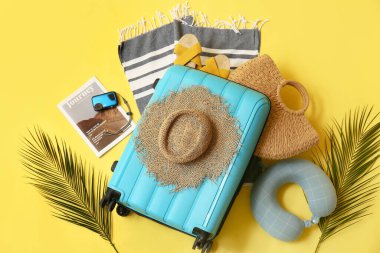 Çantalı kompozisyon, tropikal yapraklar ve sarı arka planda plaj aksesuarları.