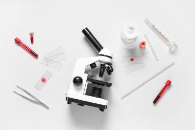 Beyaz arka planda kan örnekleri olan modern mikroskop ve test tüpleri.