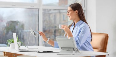 Ofiste tablet bilgisayar ve kahve fincanıyla çalışan güzel bir sekreter.