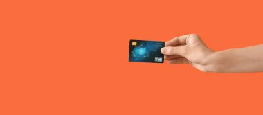 Turuncu arka planda kredi kartı olan el.