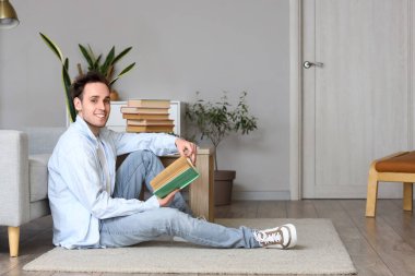 Genç adam evde yerde kitap okuyor.