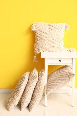 Sarı duvarın yanında şık yastıklı bir masa.