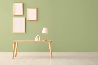 Yeşil duvarın yanında lamba ve dekor olan ahşap sehpa.