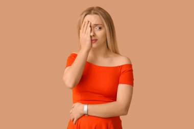 Genç hamile kadın bej arka planda facepalm yapıyor.