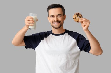 Lezzetli kurabiyesi ve gri arka planda bir bardak sütü olan yakışıklı bir adam.