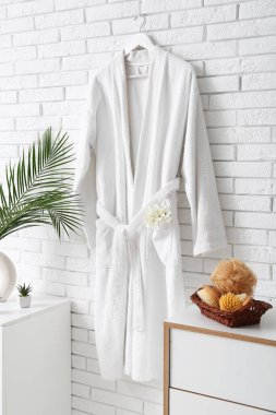Duvarda asılı beyaz bornoz ve banyodaki çekmecelerde farklı banyo malzemeleri.
