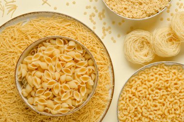 Bej arka planda farklı türde pişmemiş makarna içeren kaseler.