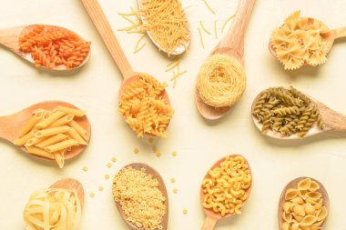 Tahta kaşıklar ve açık bej arka planda farklı ham makarnalar.