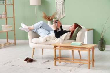 Evdeki kanepede dergi okuyan genç bir kadın.