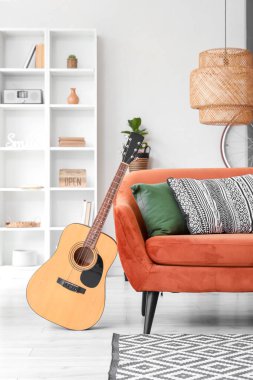 Oturma odasının içinde kahverengi kanepe, lamba ve akustik gitar var.