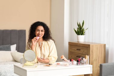 Güzel, genç, mutlu, Afro-Amerikan bir kadın. Sünger ve allık ile evde makyaj yapıyor.