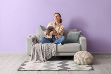 Evdeki rahat koltukta dergi okuyan genç bir kadın.