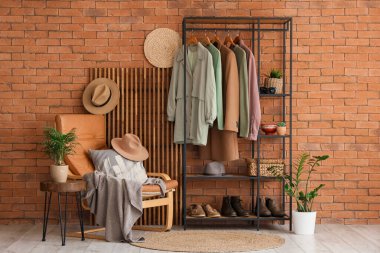 Portakal rengi tuğla duvarın yanında elbise askısı ve koltuğu olan modern soyunma odasının içinde.