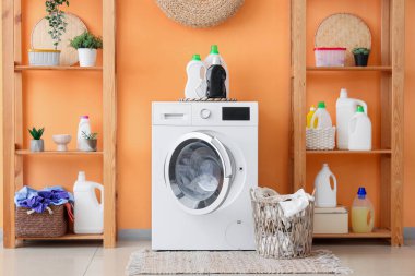 Çağdaş çamaşır makinesi ve çamaşır deterjanı ile turuncu duvarın yanındaki oda.