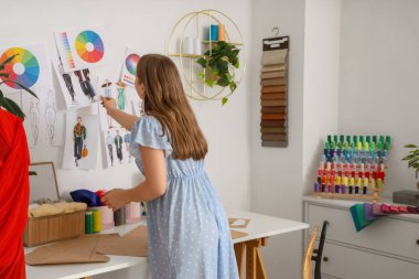 Duvarda çizimleri olan atölyede çalışan kadın terzi.