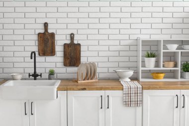 Mutfak tezgahındaki aletler beyaz tuğla duvarın yanında.