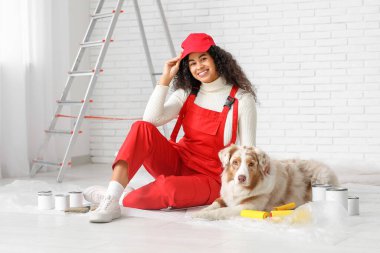 Üniformalı mutlu Afro-Amerikan ressam ve evde tamirat sırasında oturan sevimli Avustralya çoban köpeği.