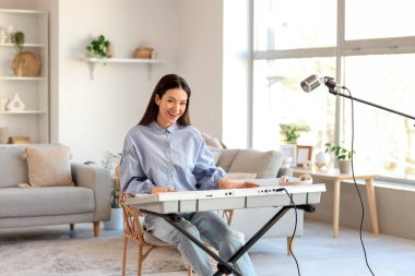 Gülümseyen genç kadın evde sentezleyici çalıyor.