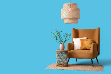 Vazoda bambu saplı masa, koltuk, halı ve lamba mavi arka planda.
