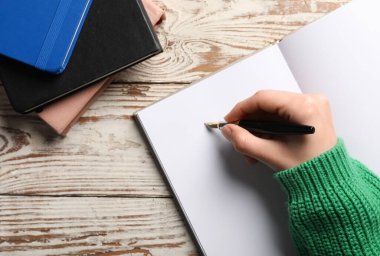 Kadın açık tahta zemin üzerine boş bir deftere bir şeyler yazıyor, yakın plan.