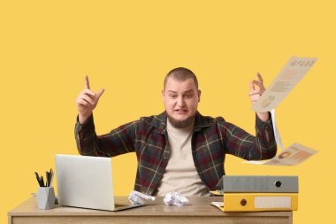 Laptoplu ve belgeli öfkeli genç adam sarı arka planda oturuyor.