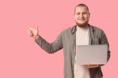 Bilgisayarlı genç adam pembe arka planda bir şeye bakıyor.