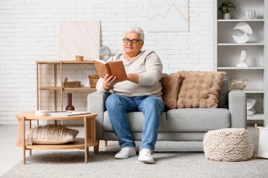 Yakışıklı son sınıf öğrencisi kitap okuyor ve oturma odasında kanepede oturuyor.