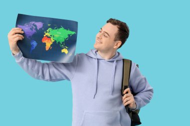 Mavi arka planda dünya haritası ve sırt çantası olan genç bir adam. Seyahat kavramı